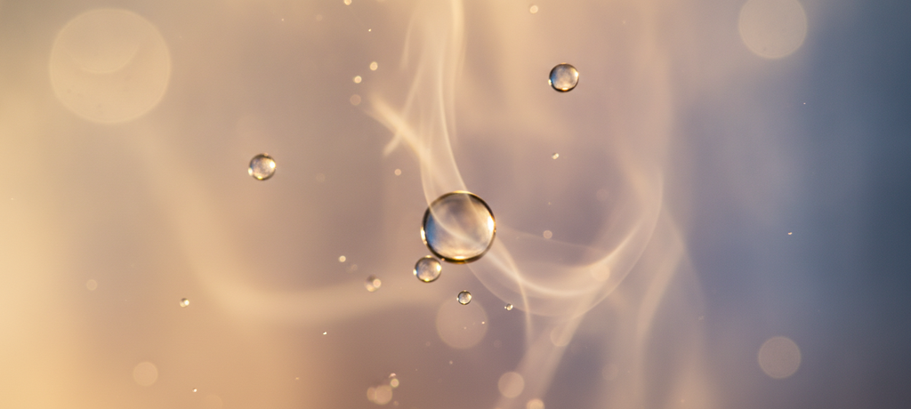 Close-up abstract representation of water droplets and gentle steam mingling in warm ambient light, conveying warmth and stillness, soft golden and cool blue tones blending together, no text, no visible objects or branding